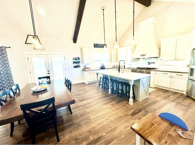 kitchen with a kitchen island with sink, custom exhaust hood, light wood-type flooring, a kitchen bar, and beam ceiling