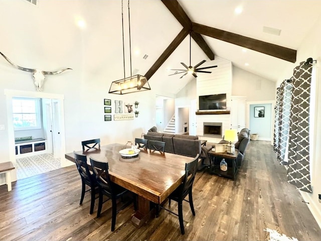 dining space featuring beam ceiling, dark wood-style flooring, a fireplace, high vaulted ceiling, and stairs