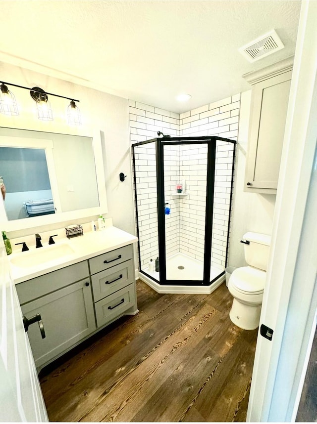 bathroom with toilet, wood finished floors, vanity, visible vents, and a shower stall