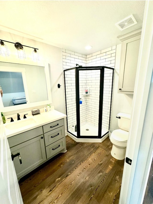 full bath featuring visible vents, toilet, wood finished floors, vanity, and a shower stall