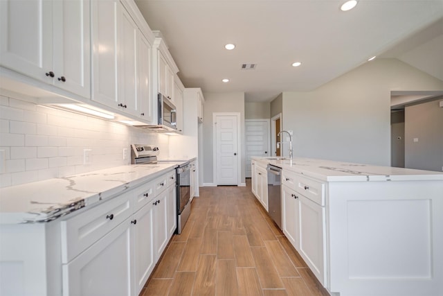 kitchen with stainless steel appliances, visible vents, white cabinetry, decorative backsplash, and light wood finished floors