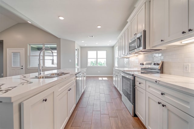 kitchen featuring wood finish floors, backsplash, appliances with stainless steel finishes, white cabinets, and a sink