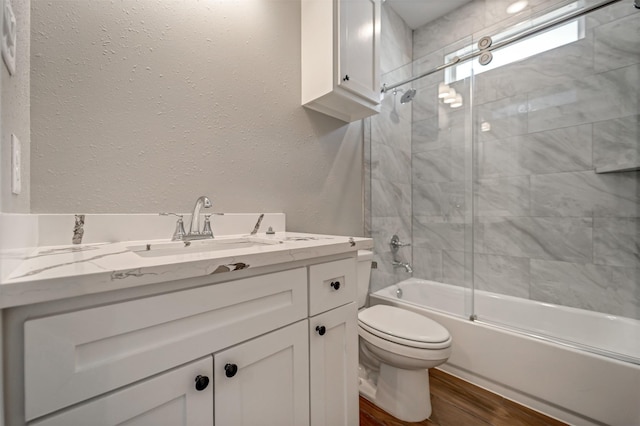 full bathroom with toilet, a textured wall, wood finished floors, and vanity