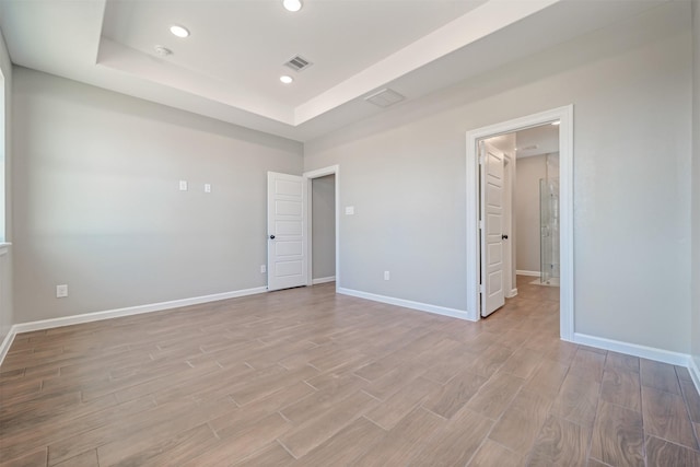 empty room with visible vents, baseboards, a raised ceiling, light wood-type flooring, and recessed lighting