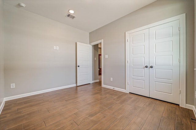 unfurnished bedroom featuring a closet, wood finished floors, visible vents, and baseboards