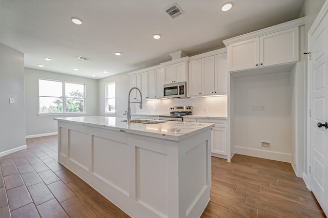 kitchen with white cabinets, stainless steel appliances, a sink, and an island with sink