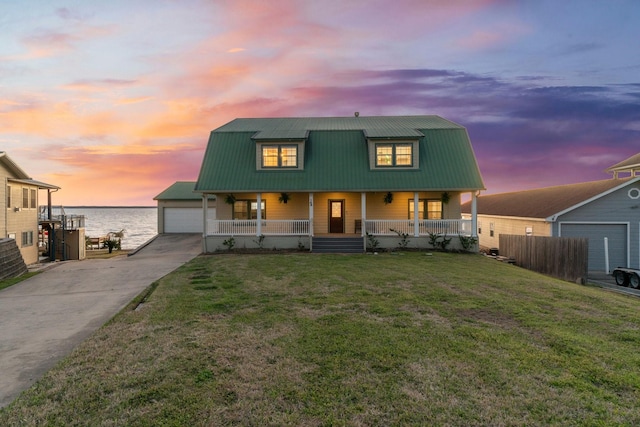 dutch colonial featuring covered porch, a water view, a front yard, metal roof, and a garage