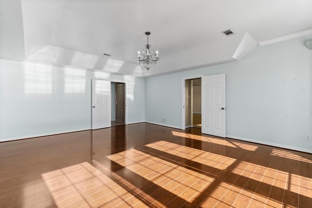 spare room featuring wood finished floors, visible vents, baseboards, a raised ceiling, and an inviting chandelier