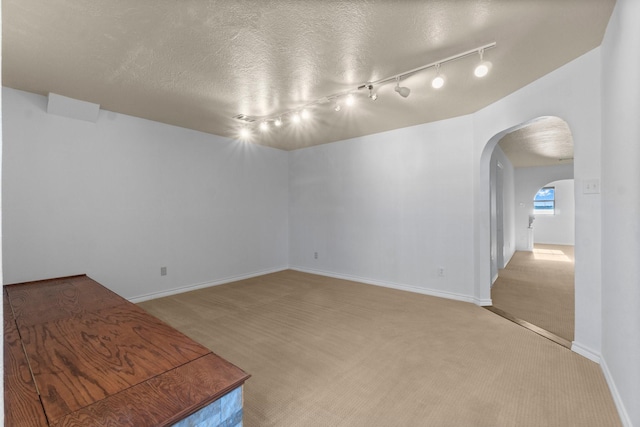 empty room featuring arched walkways, a textured ceiling, baseboards, and light colored carpet