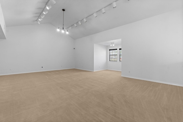 empty room featuring rail lighting, light carpet, vaulted ceiling, and baseboards