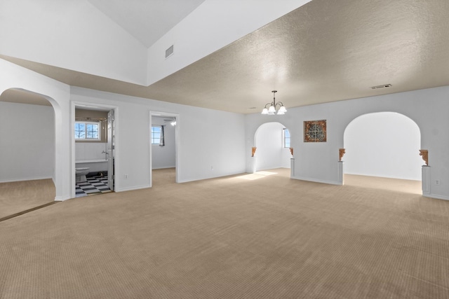 unfurnished living room with arched walkways, a textured ceiling, visible vents, and light colored carpet