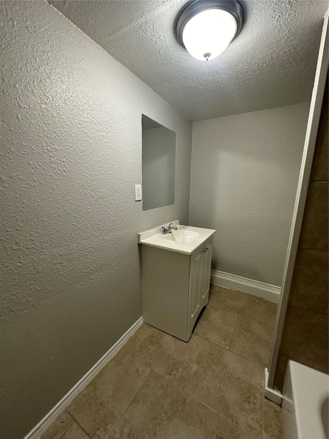 bathroom featuring vanity, baseboards, a textured ceiling, and a textured wall