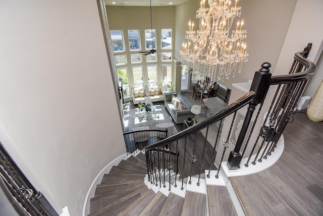 staircase featuring ceiling fan with notable chandelier, wood finished floors, a towering ceiling, and baseboards