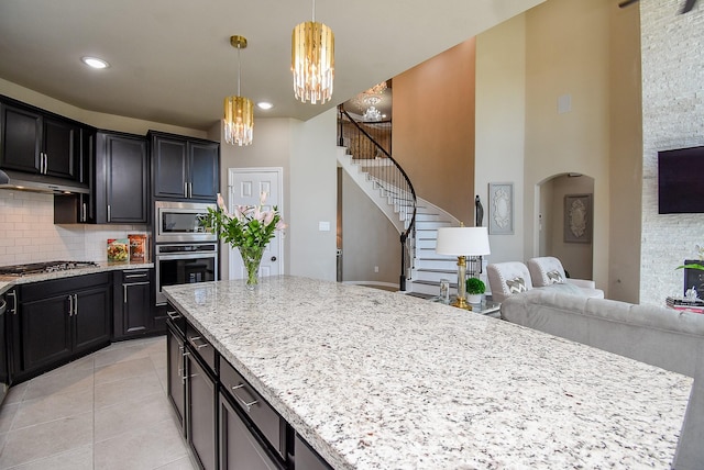 kitchen featuring arched walkways, light tile patterned flooring, under cabinet range hood, appliances with stainless steel finishes, and decorative backsplash