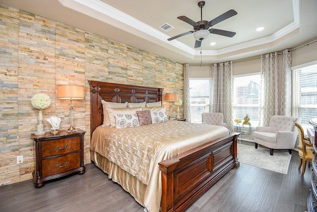 bedroom with visible vents, ceiling fan, ornamental molding, wood finished floors, and a tray ceiling