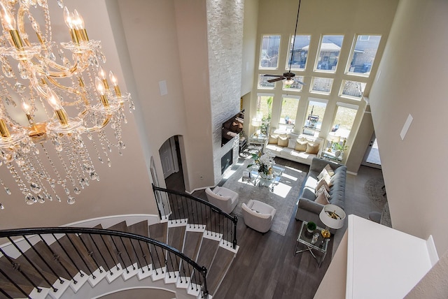 living room featuring wood finished floors, stairs, a high ceiling, a fireplace, and ceiling fan with notable chandelier