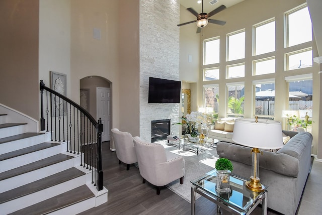 living area featuring arched walkways, visible vents, a stone fireplace, wood finished floors, and stairs