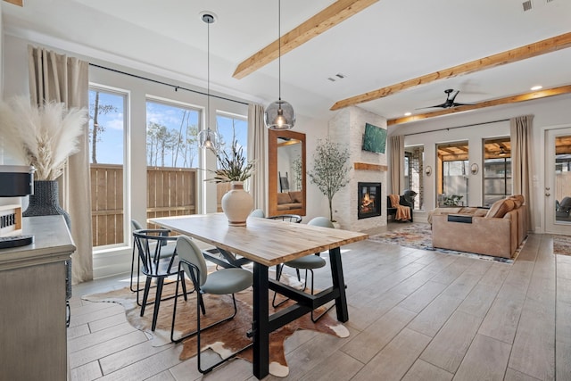 dining room featuring light wood finished floors, beamed ceiling, a fireplace, and visible vents