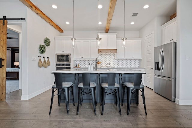 kitchen with a barn door, stainless steel appliances, visible vents, white cabinetry, and backsplash