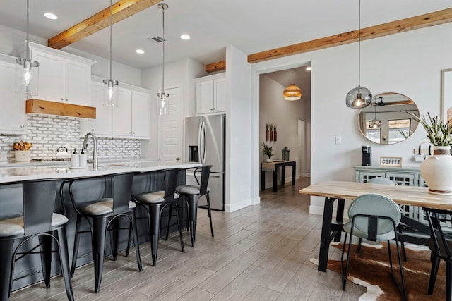 kitchen featuring beam ceiling, stainless steel refrigerator with ice dispenser, a breakfast bar area, tasteful backsplash, and light countertops