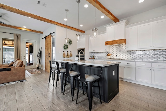 kitchen with a barn door, a sink, visible vents, backsplash, and a kitchen bar