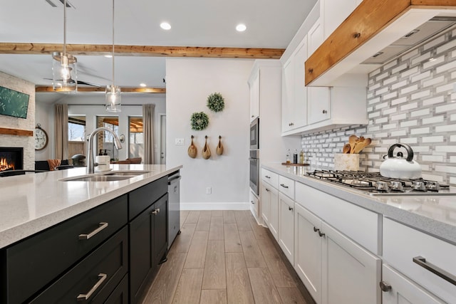 kitchen with dark cabinets, under cabinet range hood, a sink, appliances with stainless steel finishes, and decorative backsplash