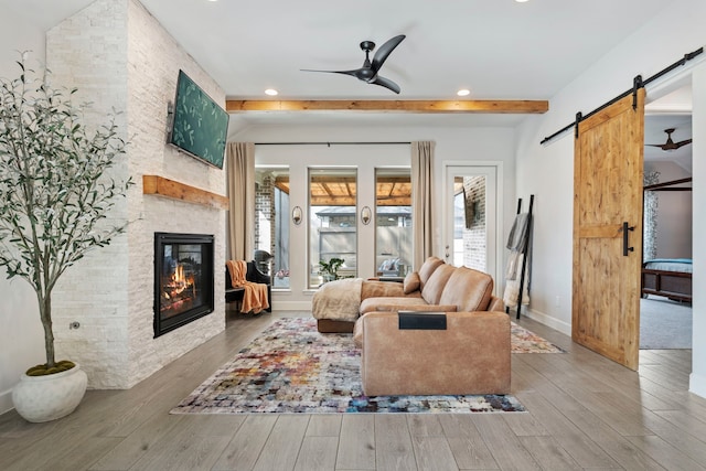 living room with a barn door, ceiling fan, wood finished floors, beamed ceiling, and a fireplace