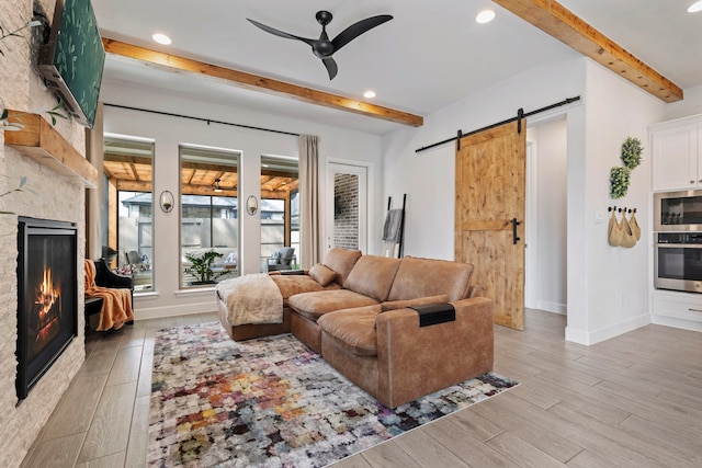 living area featuring light wood finished floors, a barn door, a fireplace, and beam ceiling