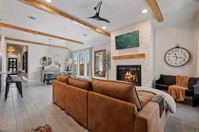 living room featuring baseboards, ceiling fan, beamed ceiling, light wood-style floors, and a fireplace