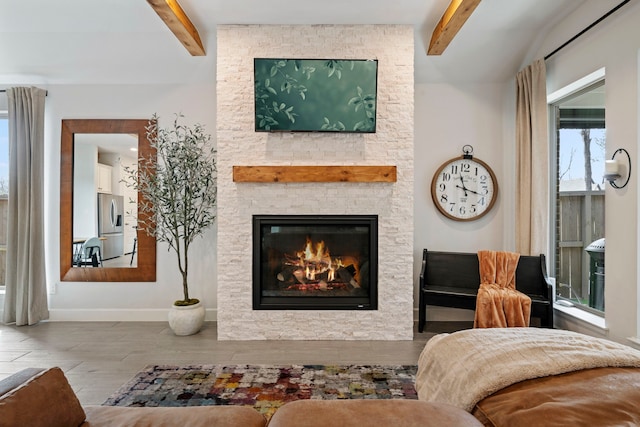 living area with beamed ceiling, a stone fireplace, baseboards, and wood finished floors