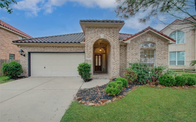 mediterranean / spanish-style home with brick siding, driveway, a tiled roof, and an attached garage