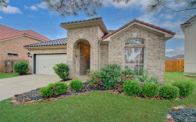 mediterranean / spanish home with a garage, concrete driveway, a tile roof, fence, and a front lawn