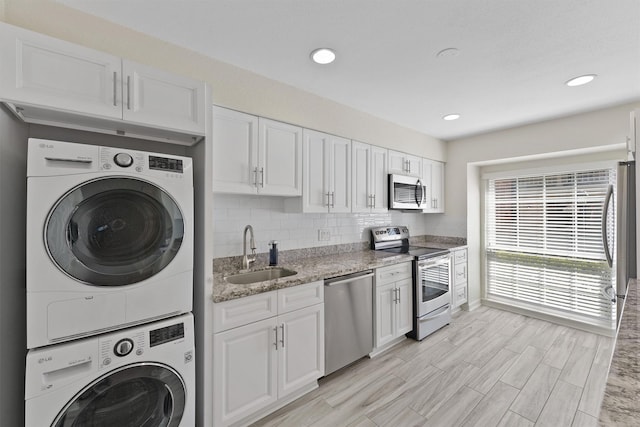 kitchen with stacked washer / dryer, white cabinetry, stainless steel appliances, and a sink