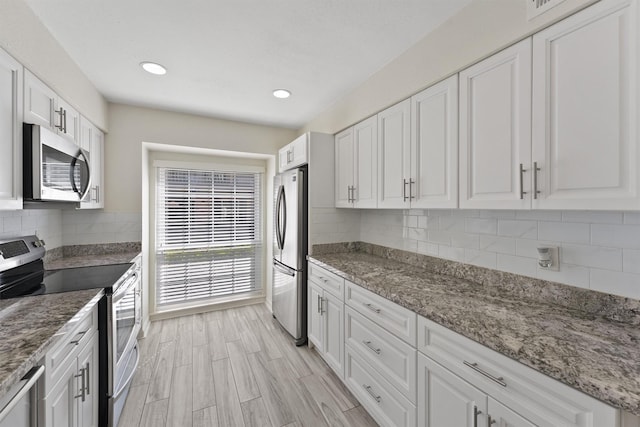 kitchen with light stone counters, tasteful backsplash, appliances with stainless steel finishes, white cabinetry, and light wood-type flooring