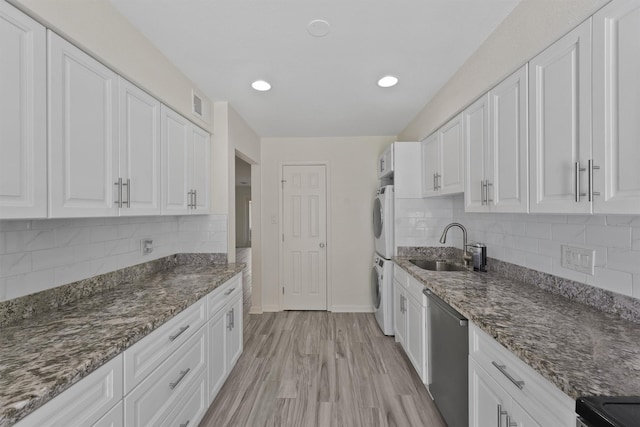 kitchen featuring dishwasher, stacked washer / dryer, a sink, and white cabinets