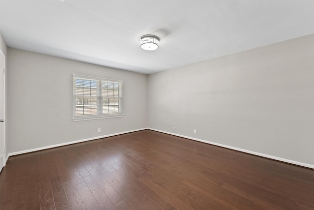 spare room featuring baseboards and dark wood-type flooring