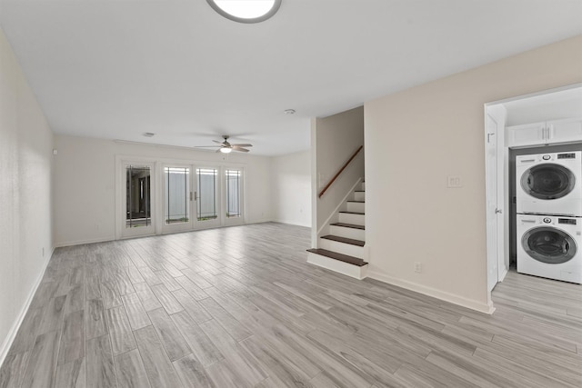 unfurnished living room featuring light wood-style floors, stacked washer / dryer, ceiling fan, baseboards, and stairs