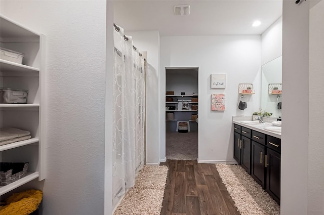 full bath featuring a spacious closet, visible vents, double vanity, wood finished floors, and a sink