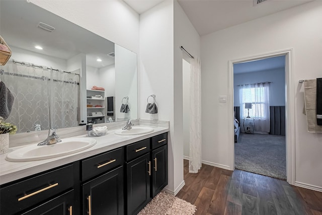 ensuite bathroom with double vanity, wood finished floors, visible vents, and a sink