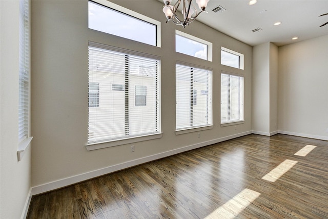 spare room featuring visible vents, baseboards, an inviting chandelier, and wood finished floors