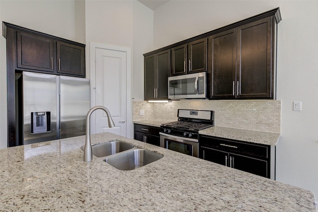 kitchen with light stone counters, a sink, dark brown cabinetry, appliances with stainless steel finishes, and tasteful backsplash