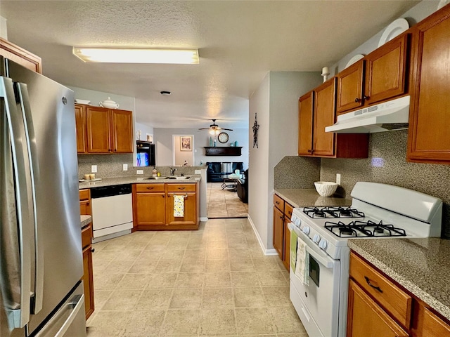 kitchen featuring under cabinet range hood, a peninsula, white appliances, a sink, and brown cabinets