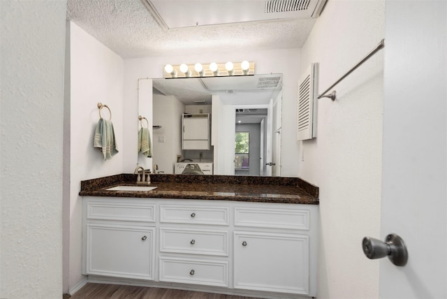 bathroom with stacked washer and dryer, visible vents, wood finished floors, a textured ceiling, and vanity