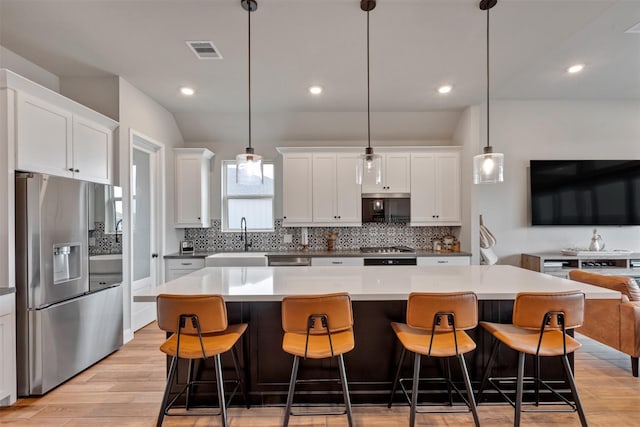 kitchen with visible vents, a sink, decorative backsplash, light wood-style floors, and appliances with stainless steel finishes