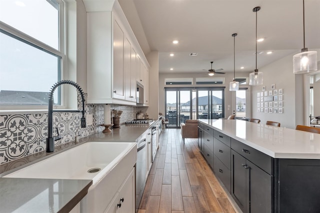 kitchen with stainless steel appliances, a sink, white cabinets, tasteful backsplash, and light wood-type flooring