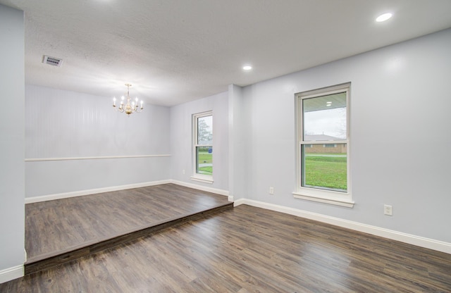 unfurnished room featuring dark wood-style floors, baseboards, visible vents, and a notable chandelier