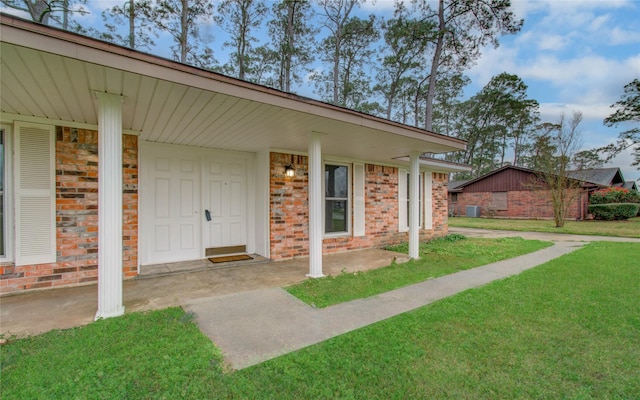 view of exterior entry featuring brick siding and a lawn