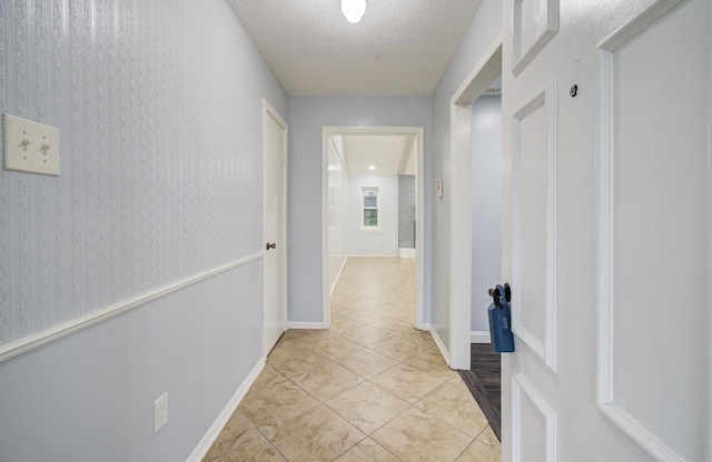 hall featuring light tile patterned flooring, a textured ceiling, and baseboards