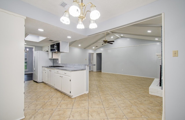 kitchen with stainless steel microwave, freestanding refrigerator, white cabinets, vaulted ceiling with skylight, and ceiling fan with notable chandelier