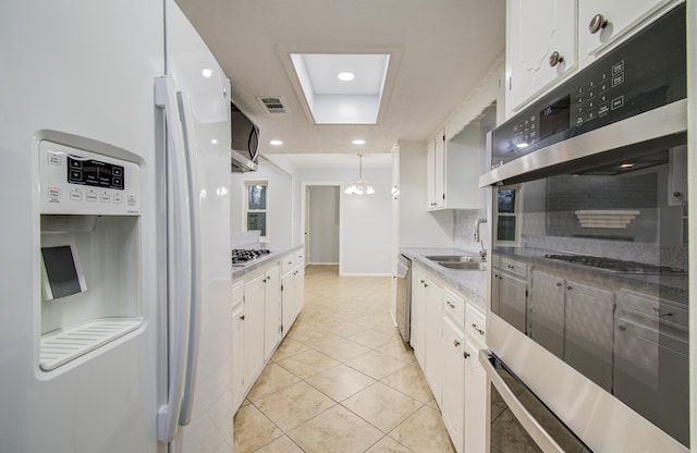 kitchen featuring white cabinets, appliances with stainless steel finishes, a sink, backsplash, and light tile patterned flooring